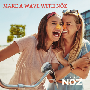 A mother and daughter hug on the beach while laughing, they have colored sunblock on their noses