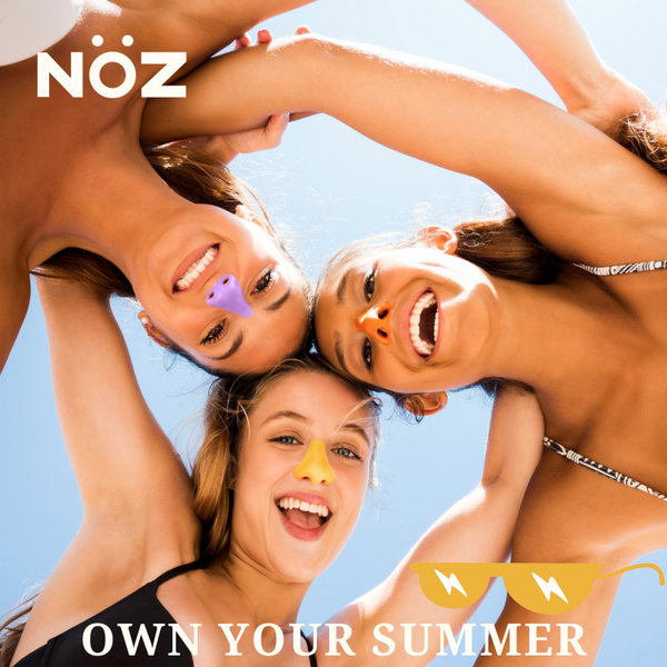 three girl best friends wearing swimsuits with colored sunblock on their noses huddle in a circle and look down at the camera, the caption reads "own your summer".